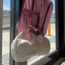 Pink backpack with a cap and magnetic hat clip hanging on a glass door.
