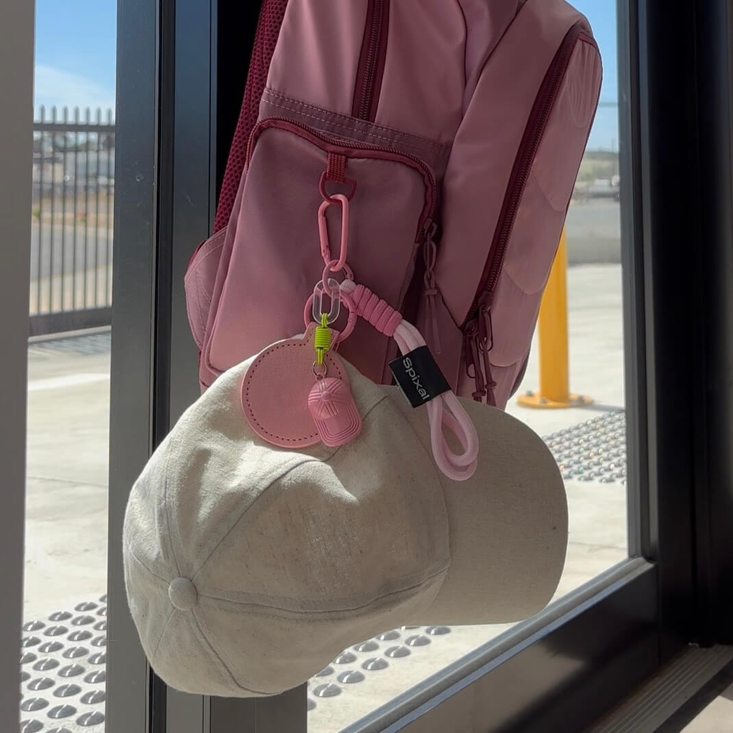 Pink backpack with a cap and magnetic hat clip hanging on a glass door.