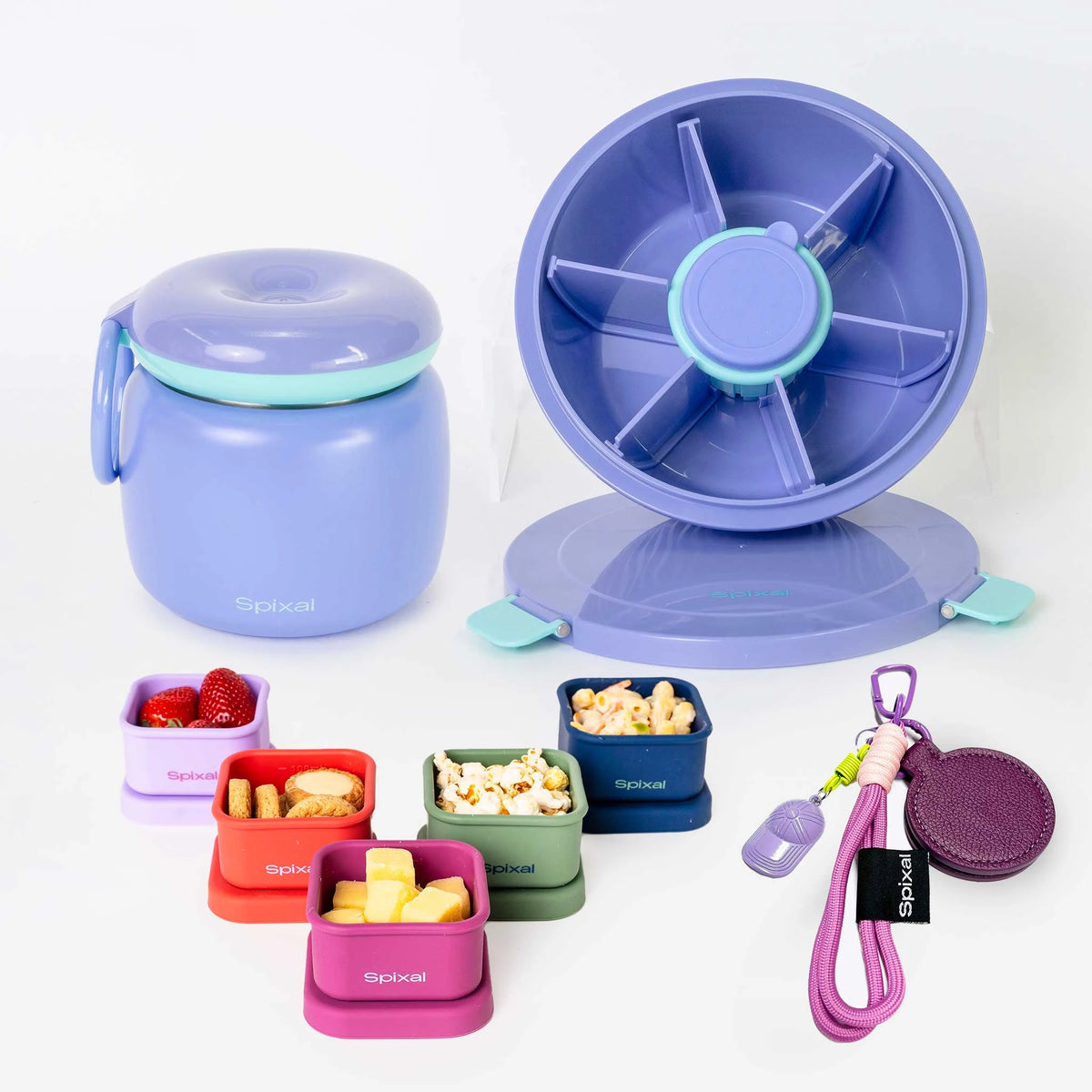 A set of Spixal lunch containers and accessories on a clean white background, including a purple insulated food jar with teal trim, a purple spinner lid, smaller colourful containers with food samples, a purple magnetic hat clip. Main image