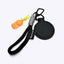 A black circular leather magnetic hat clip accessory with a black wrist loop, black carabiner, gray cord wrap, a small orange cap-shaped charm, and a black tag with the brand name 'spixal' printed in white, shown on a light gray background.