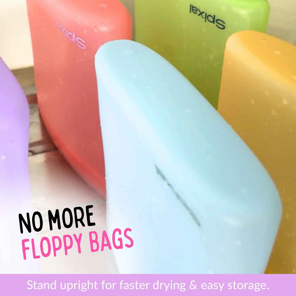 Five colourful Spixal silicone snack and sandwich bags in purple, red, light blue, green, and yellow, standing upright to show their shape and water-droplet finish as they sit to dry. Text overlays read 'NO MORE FLOPPY BAGS' and 'Stand upright for faster drying & easy storage '.