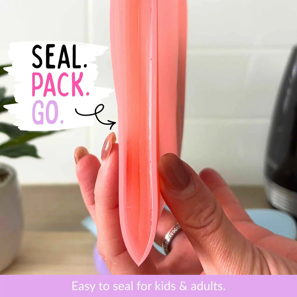 A hand holds a red silicone snack and sandwich bag in a kitchen setting, with text overlays reading 'SEAL. PACK. GO' Easy to seal for kids and adults