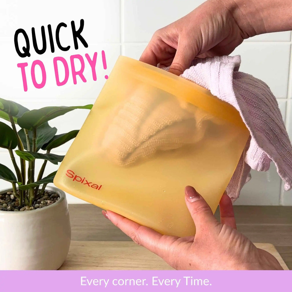 A person holds a yellow silicone drying bag with the brand name 'Spixal' printed in red, drying it with a pink tea towel.