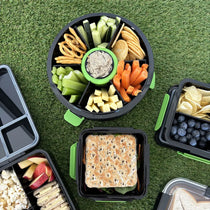 Black Roundie bento lunch box packed with snacks next to black lunch boxes