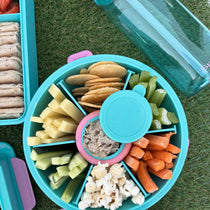 Teal Roundie bento with snacks in six compartments, top view on grass